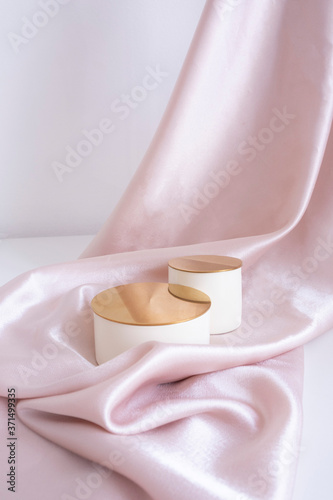 two beige podium - top hat with a gold top on a pink satin background with folds. Luxurious showcase for advertising and product promotion..