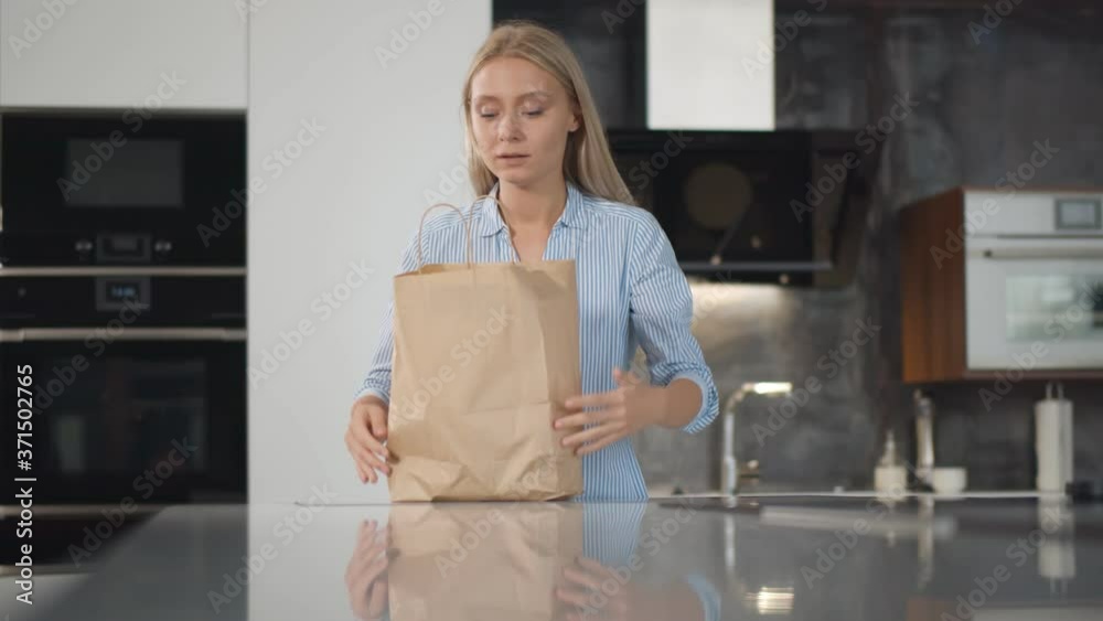 Young woman unpacking the products from paper bag while standing in modern kitchen at home Young woman unpacking the products from paper bag while standing in modern kitchen at home