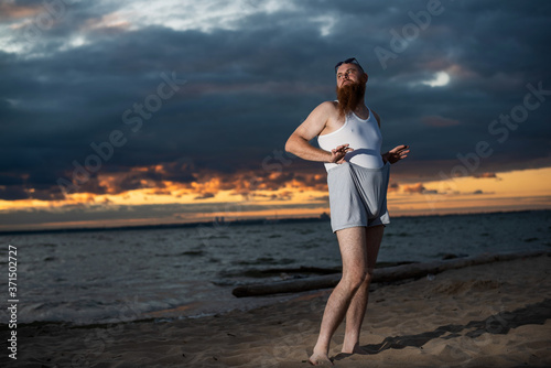 Платно A brutal bald man posing on the beach at sunset parody glamorous chick