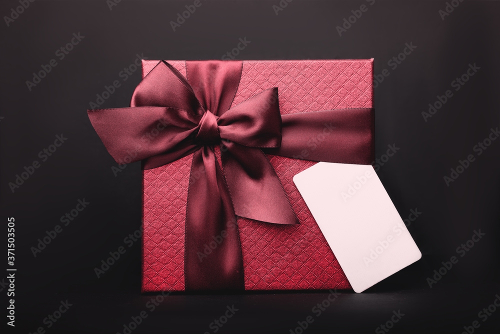 A beautiful red gift box with an empty tag on the black background. Copy Space. A beautiful red gift box with an empty tag on the black background. Copy Space.
