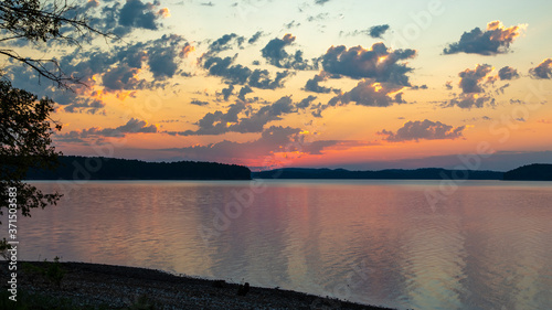 sun rising into clouds over lake and mountains