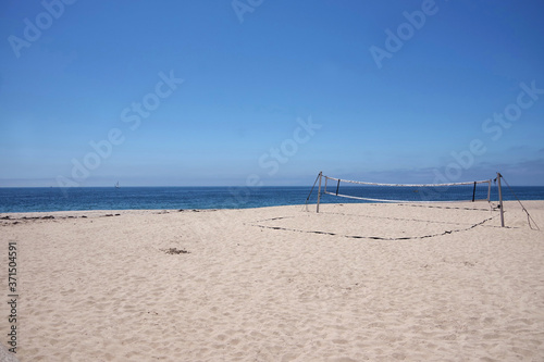 View of a beach volleyball net at an empty beach in bright summer sunlight with blue sky and some fog clouds at the horizon over the ocean