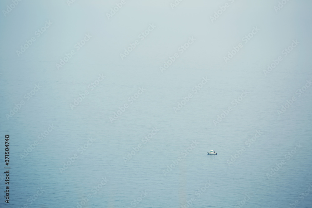 Alone boat ship in foggy sea, single sail on a calm blue sea.