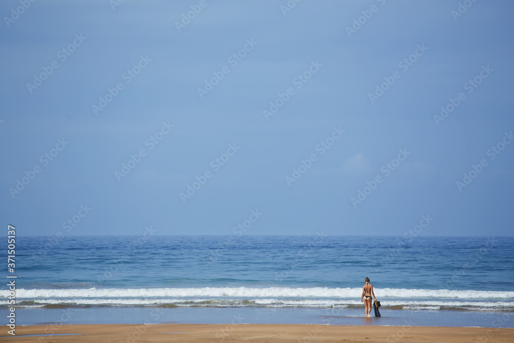 Young woman in bikini standing against ocean enjoying beautiful view and sun