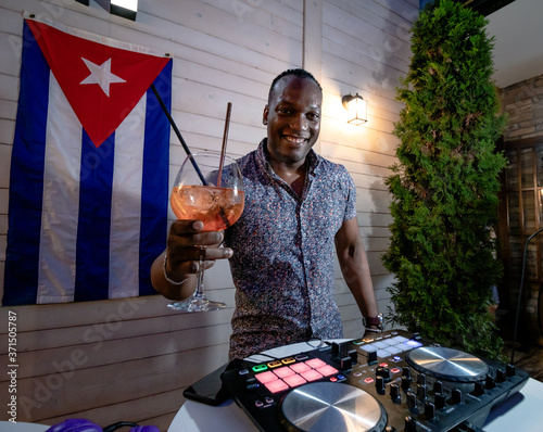 Photography Cuban disc jockey drinking cocktail and playing music on a modern dj turntable mixer equipment
