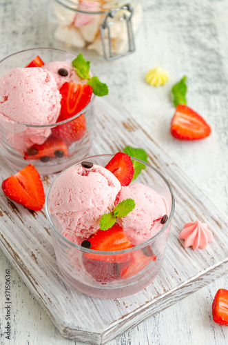 Strawberry ice cream in a glass with fresh strawberries, chocolate drops and mint on a board on a light wooden background. Vertical, copy space.