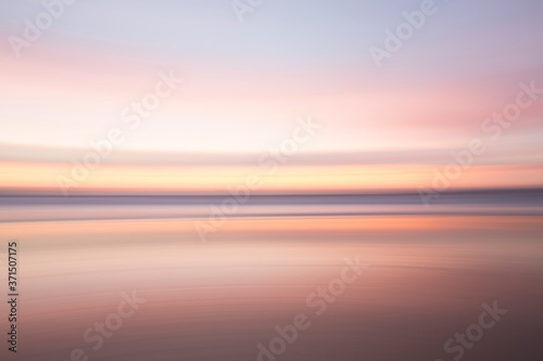 Defocused view of ocean waves on beach under sunset sky photo