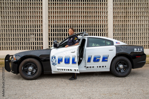 Policewoman standing in door of Police car looking towards camera smiling 