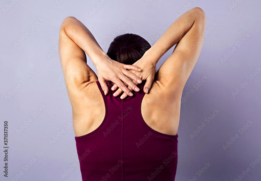 Young strong sporty woman suffering from neck pain. Touching and massaging the hands. Sports exercising injury. Closeup portrait on purple background. Back Young strong sporty woman suffering from neck pain. Touching and massaging the hands. Sports exercising injury. Closeup portrait on purple background. Back
