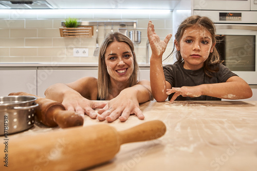 Playful mother and daughter with messy faces sitting at table in kitchen
