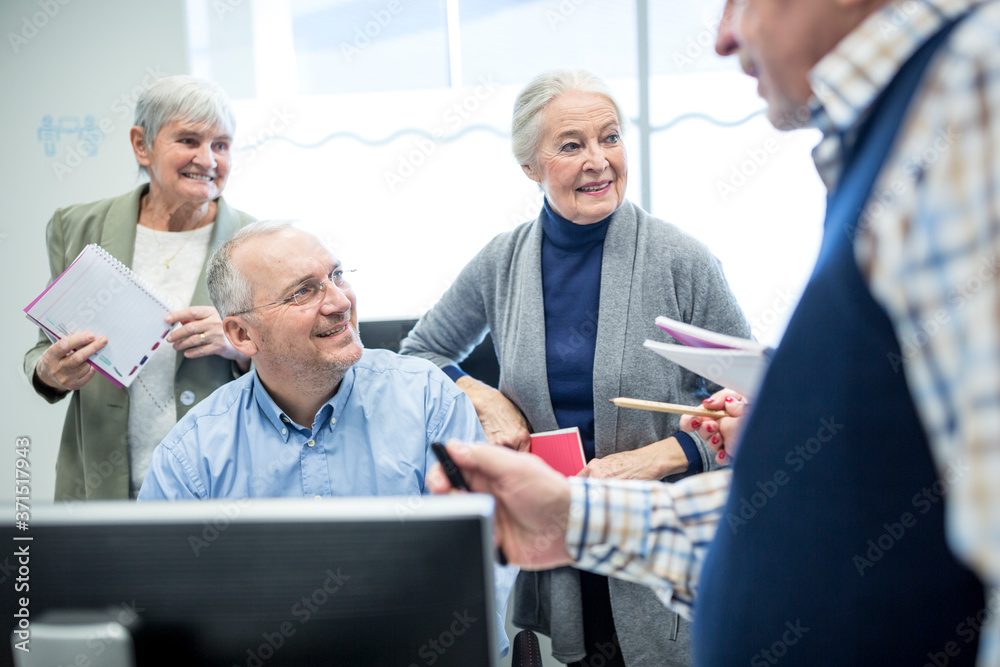 Active seniors attending computer course, watching instructor and taking notes Active seniors attending computer course, watching instructor and taking notes