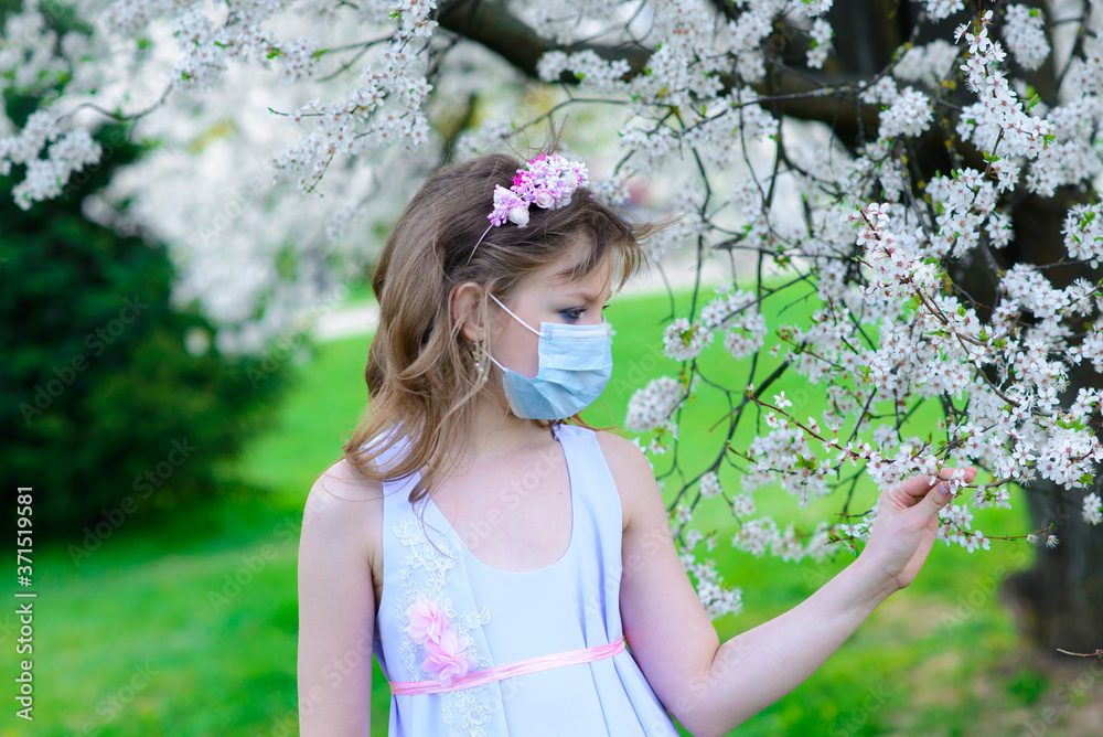 Lonely teenage girl wearing protection medicine mask against virus and allergy enjoying spring flower blossom in blooming garden Lonely teenage girl wearing protection medicine mask against virus and allergy enjoying spring flower blossom in blooming garden