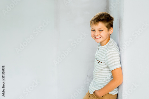 Emotional and smiling Child.On the background of a white concrete wall, baby fashion concept. cute boy outdoors in summer