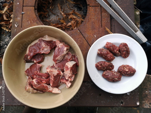 Schale mit rohem Lammfleisch, Teller mit Frikadellen und Grillzange auf einem rostigen Holzkohlegrill bei einem Barbecue in Rudersau bei Rottenbuch im Landkreis Weilheim-Schongau in Oberbayern photo