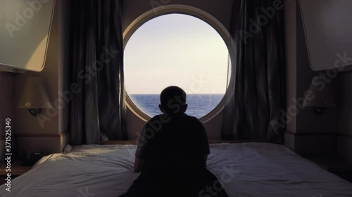 Man lays on bed in front of the window in stateroom onboard cruise ship