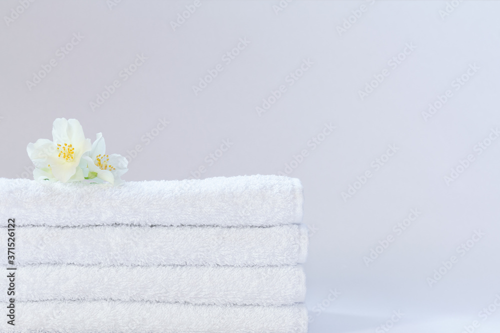 Four white neatly folded terry towels with a jasmine flower on a light background. Four white neatly folded terry towels with a jasmine flower on a light background.