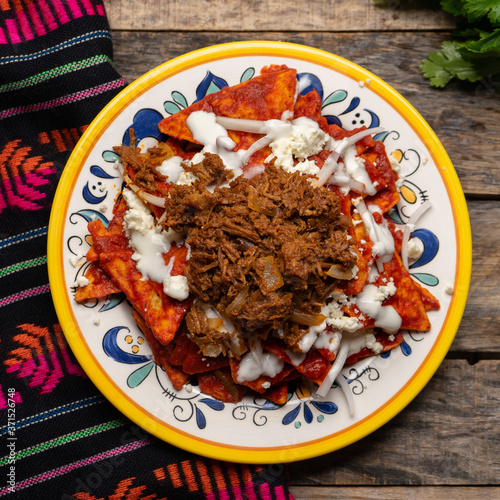 Mexican red chilaquiles with chilorio and cheese on wooden background photo