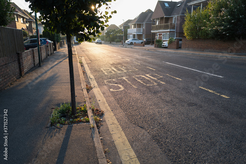 Φωτογραφία Yellow painted bus stop sign on a residential road on a summer evening as the sunlight shines though the leave of a roadside tree and illuminates the tarmac