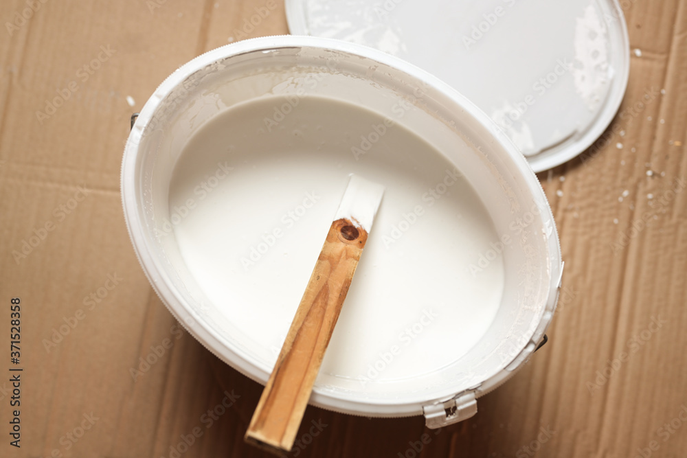 View into a bucket with white wall paint and a wooden stirring stick while renovation View into a bucket with white wall paint and a wooden stirring stick while renovation