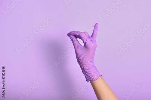 a woman's hand in a sterile lilac glove shows a hand gesture on an isolated purple background