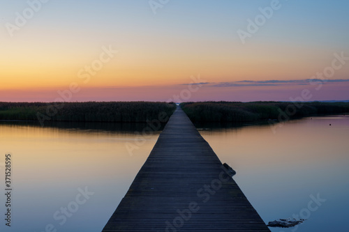 Fototapeta Naklejka Na Ścianę i Meble -  Perspective view of a wooden jetty over sea during summer sunset with reflection in the water.