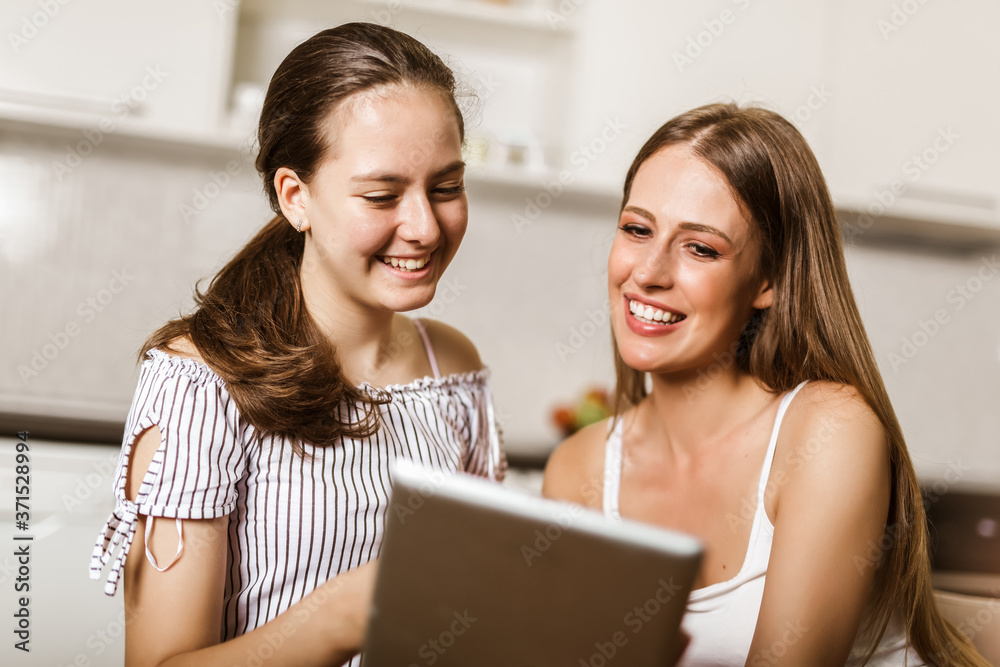 Two happy smiling female friends sharing a tablet computer as they stand close together looking at the screen Two happy smiling female friends sharing a tablet computer as they stand close together looking at the screen