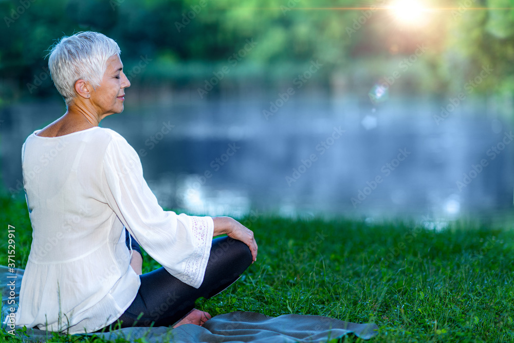 Fototapeta premium Senior woman meditating by the water