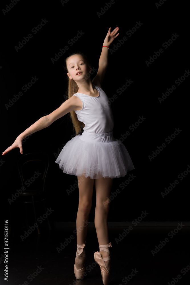 Cute little girl in a tutu and pointe shoes is dancing in the studio on a black background. Cute little girl in a tutu and pointe shoes is dancing in the studio on a black background.