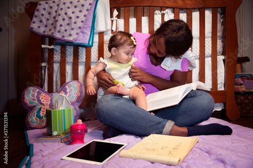 Young female nanny in nursery playing with baby on floor in front of crib  photo