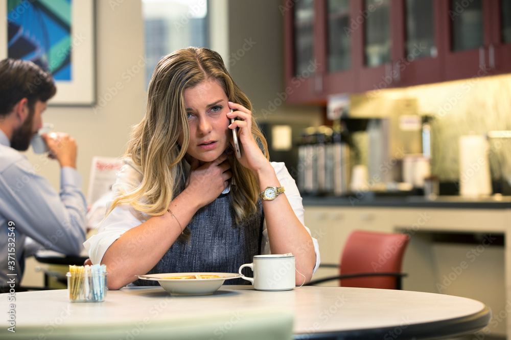 Young Caucasian woman with sore throat talking on cell phone while sitting in break area of office with lunch of soup and Hot Tea Young Caucasian woman with sore throat talking on cell phone while sitting in break area of office with lunch of soup and Hot Tea