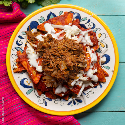 Mexican red chilaquiles with chilorio and cheese on turquoise background photo