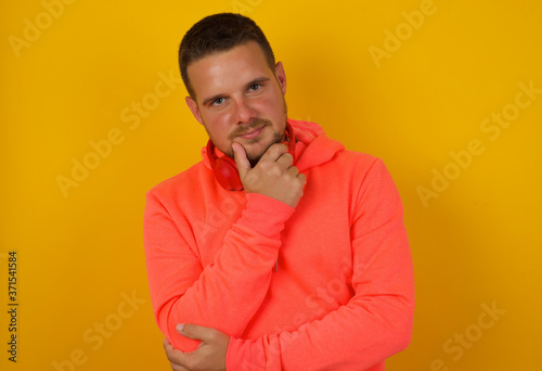 Portrait of thoughtful smiling man keeps hand under chin, looks directly at camera, listens something with interest, dressed casually, poses against gray wall. Youth concept.