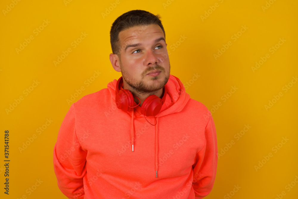 Fototapeta premium Pleasant looking young male student, looks pensively aside, plans actions after university, imagines what to do. Clever man thinks over about new project. Copy space on gray.