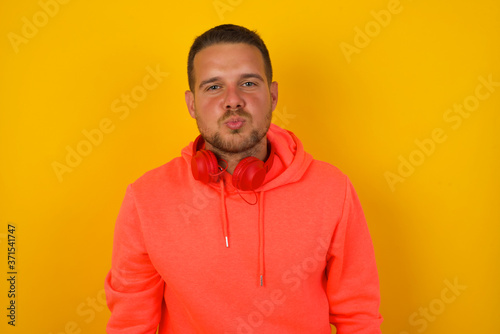 Attractive light haired male rounds lips, wears casual clothes, looks directly into camera, expresses her satisfaction, isolated over gray background. People, body language conceptâ€ 