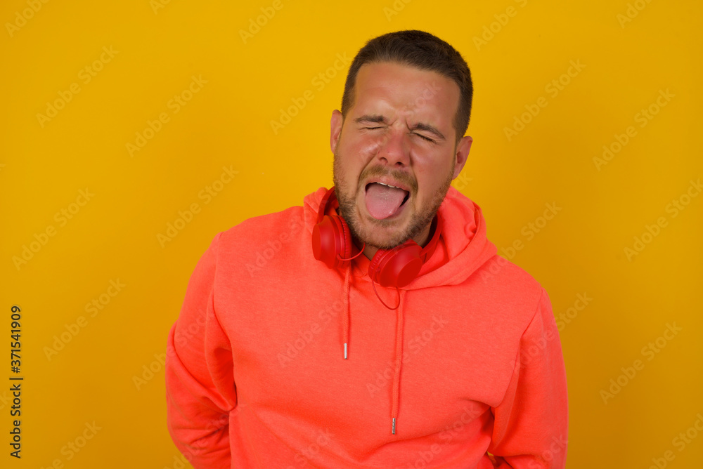 Handsome Caucasian man with happy and funny face smiling and showing tongue. Wearing casual clothes and standing against gray studio background. Handsome Caucasian man with happy and funny face smiling and showing tongue. Wearing casual clothes and standing against gray studio background.