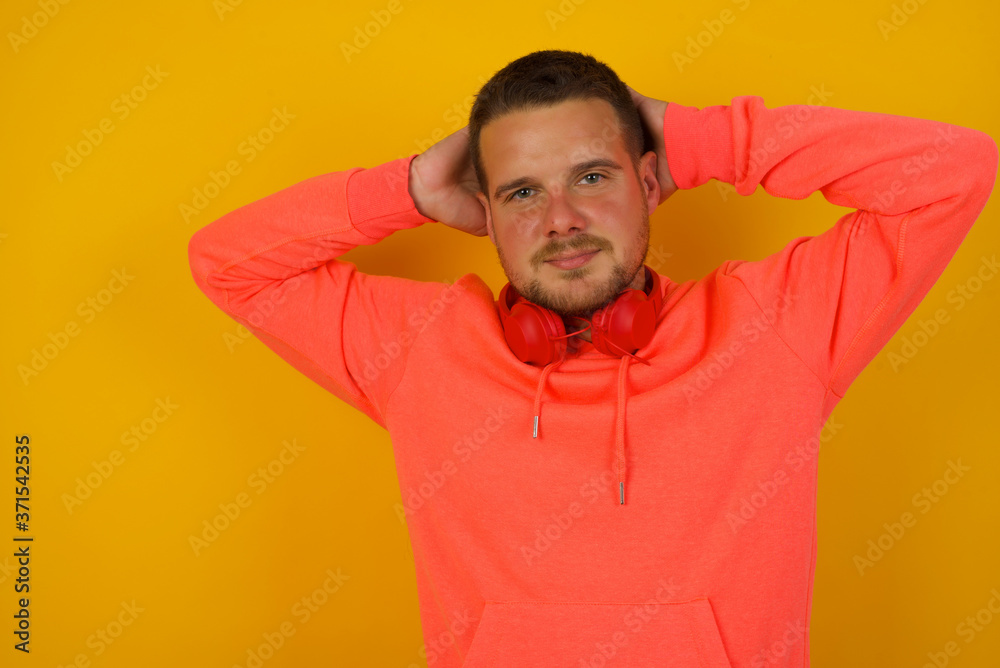 Confidence and coquettish concept. Portrait of charming young man, smiling broadly with self-assured expression while holding hands over her head. Standing against gray background. Confidence and coquettish concept. Portrait of charming young man, smiling broadly with self-assured expression while holding hands over her head. Standing against gray background.