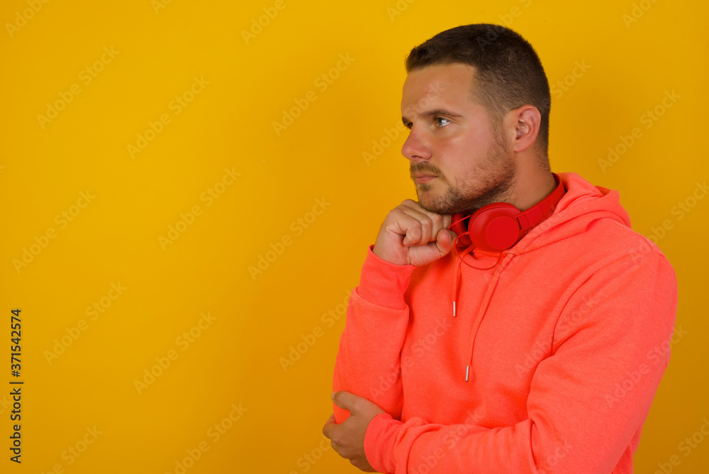 Isolated portrait of stylish young European man with hand under chin and looking sideways with doubtful and skeptical expression, suspect and doubt. Standing indoors over gray background. Isolated portrait of stylish young European man with hand under chin and looking sideways with doubtful and skeptical expression, suspect and doubt. Standing indoors over gray background.