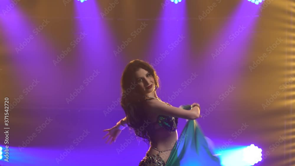 Girl in a green shiny oriental costume performs classical belly dance. Shot in a dark studio with smoke and blue neon lighting. Close up. Girl in a green shiny oriental costume performs classical belly dance. Shot in a dark studio with smoke and blue neon lighting. Close up.