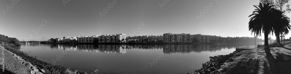 Beautiful black and white panoramic view of a river with reflections of modern apartment buildings, clear sky and trees on water, Parramatta river, Wilson Park, Sydney, New South Wales, Australia