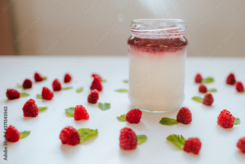 A jar of raspberry yogurt surrounded by raspberries and mint leaves A jar of raspberry yogurt surrounded by raspberries and mint leaves