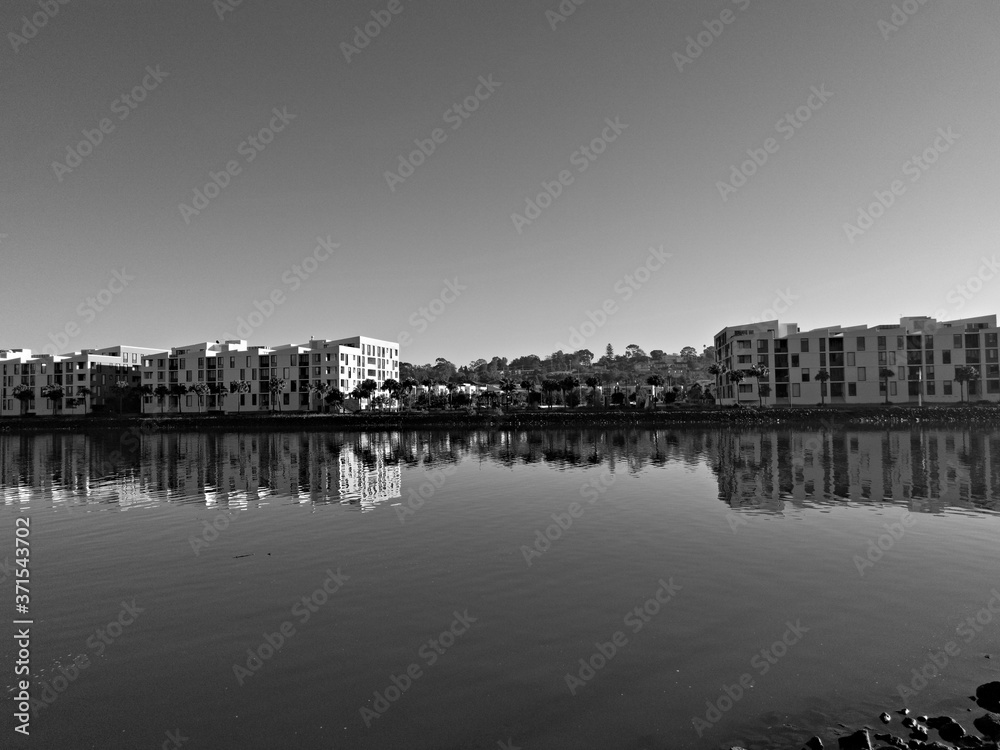 Beautiful black and white view of a river with reflections of modern apartment buildings, clear sky and trees on water, Parramatta river, Wilson Park, Silverwater, Sydney, New South Wales, Australia
