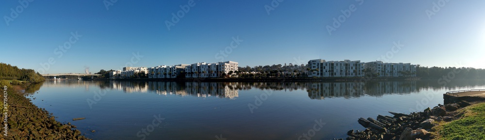 Beautiful panoramic view of a river with reflections of modern apartment buildings, deep blue sky and trees on water, Parramatta river, Wilson Park, Silverwater, Sydney, New South Wales, Australia
