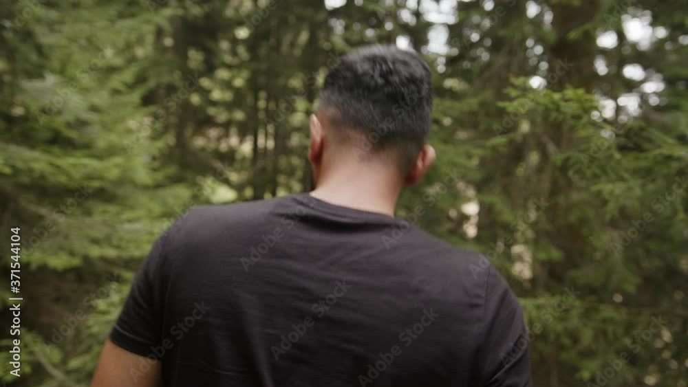 Young man wearing a black t-shirt, walking through the forest, back view Young man wearing a black t-shirt, walking through the forest, back view