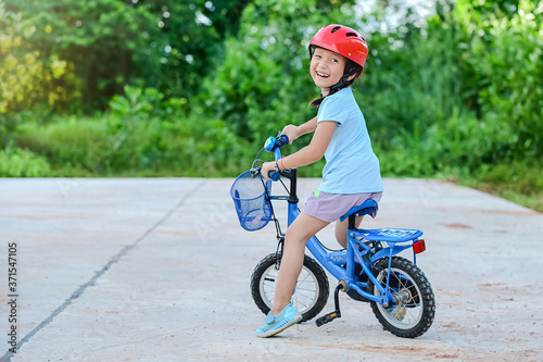 Fototapeta Naklejka Na Ścianę i Meble -  Happy child girl cycling in the park in the village for evening with sunset light exercise. Active child wearing bike helmet. Safety sports leisure with kids concept