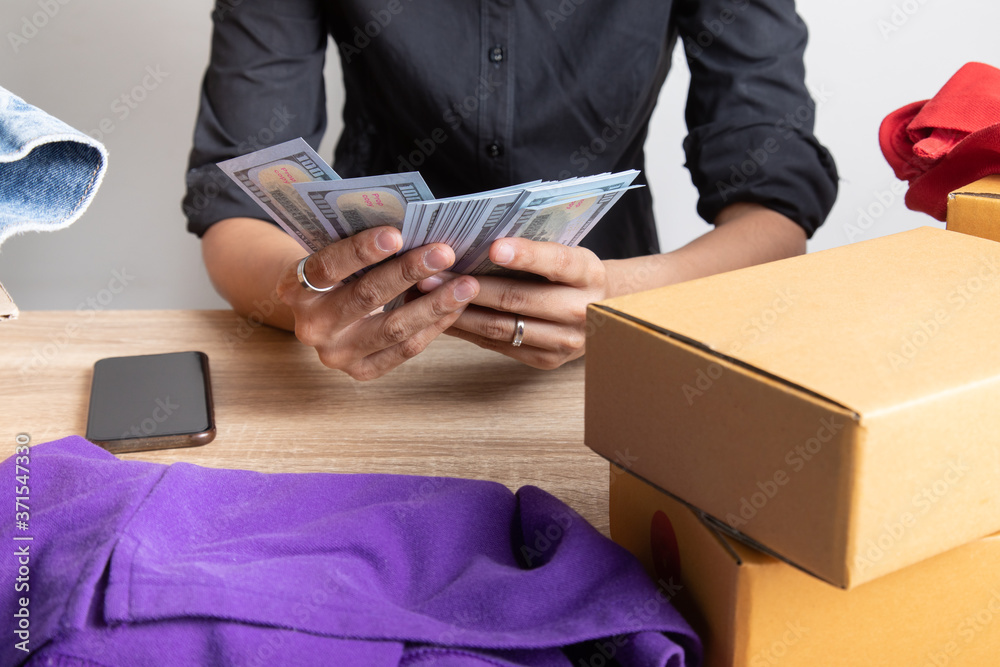 Top view shot of merchandise table with a lot of earning money (mockup banknote) in hands from e-commerce which selling products via online shows boxes and clothes for shipping to customers