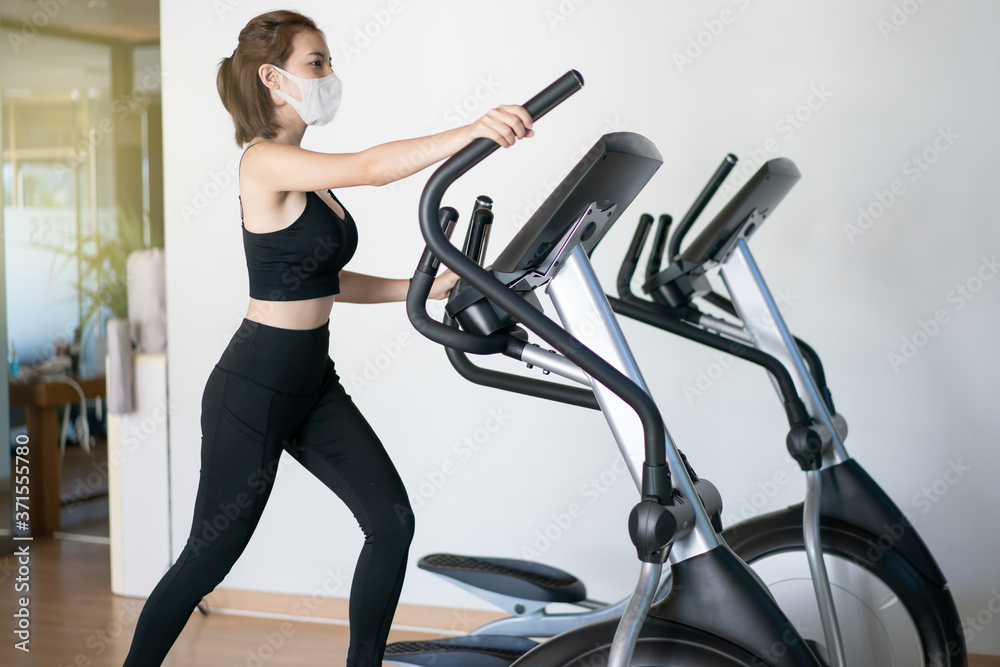 Fototapeta premium Woman wearing face mask, using an elliptical machine in a fitness center. during corona virus pandemic.