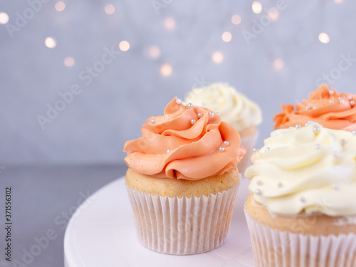 Cupcakes with orange and white cream, selective focus on blurred lights background with copy space, closeup. Celebration concept.