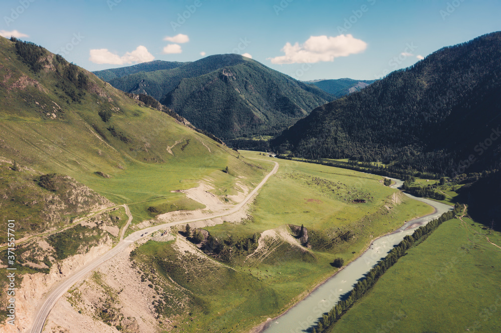Summer mountains valley with river and serpentine mountain road. Aerial drone view