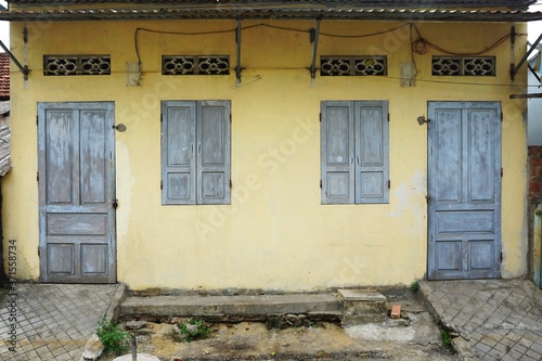 Weathered wooden doors and window shutters set in a faded yellow wall in rural Southeast Asia