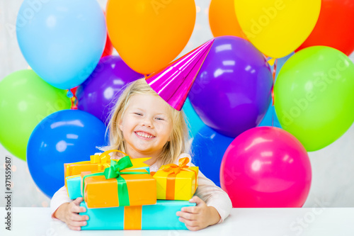Happy little girl wearing party's cap holds many gift boxes. Empty space for text
